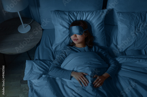people, relax and comfort concept - young asian woman in eye mask sleeping in bed at home at night