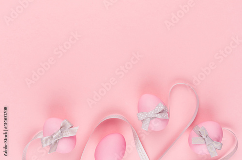 Cute easter eggs with grey curved ribbon lines as border on pastel pink background, copy space.