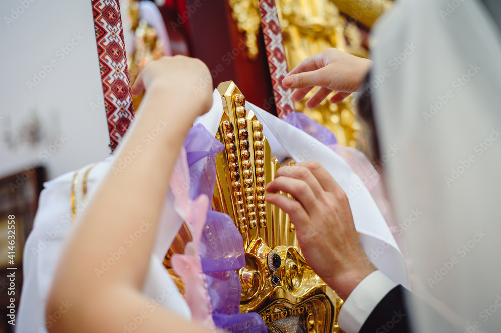 Bride and groom at a wedding ceremony in church. Brides hang a ribbon on a holy icon