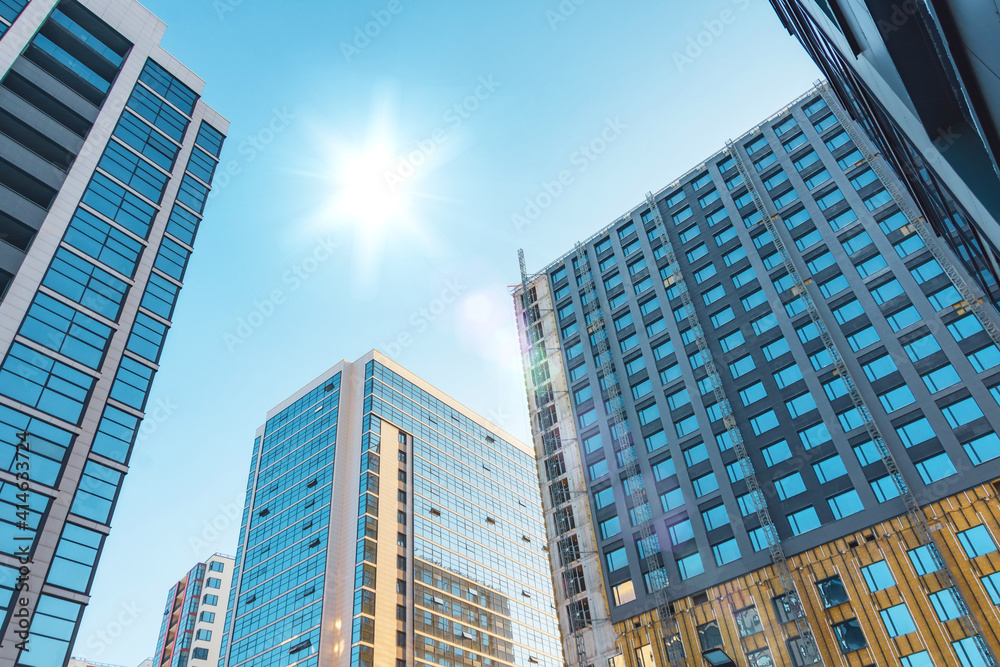 Several multi storey buildings with a glass facade and under construction with a facade section, with a bright sun in the sky. Several multi storey buildings with a glass facade and under construction with a facade section, with a bright sun in the sky.