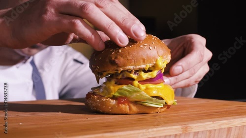 Man Preparing Tasty Burger For Dinner In Home Modern Kitchen. Chef Hands Cooking Delicious Hamburger In Fast Food Restaurant Kitchen. Cook Preparing Food In Eatery Cuisine. Cheeseburger Meal For Lunch
