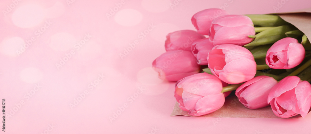 Fototapeta premium Bouquet of tulips wrapped in craft paper on pink background with space for text. Greeting card. Concept woman's or mother's day. Spring flowers background. Banner