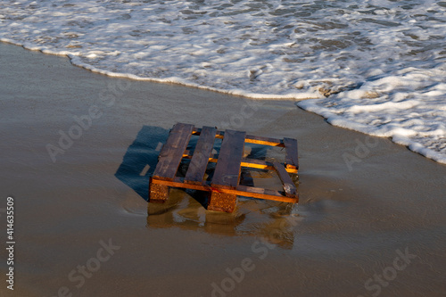 wooden pallet on the beach buried in sand bathed by the waters of the sea