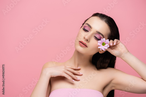 sensual young woman holding flower while looking away isolated on pink