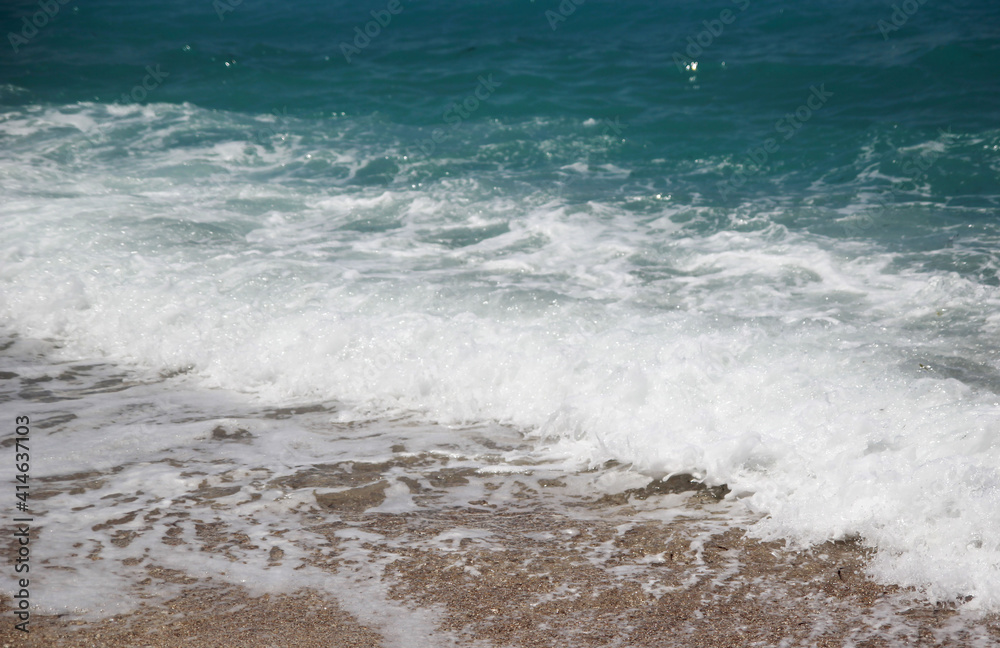 Blue wave with white foam on a sunny beach, relaxation by the sea, relaxation