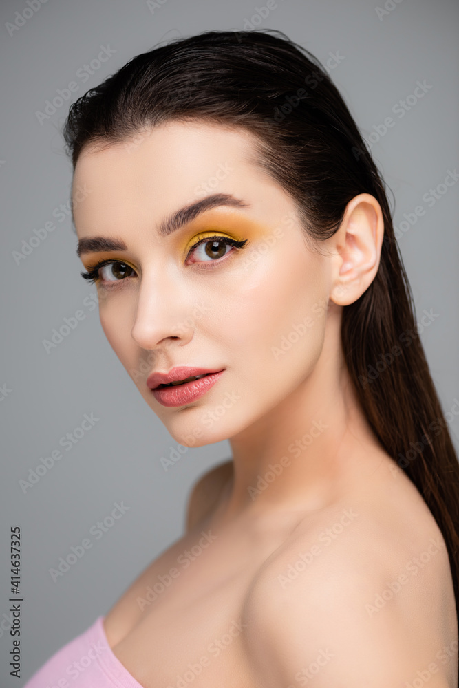young brunette woman with yellow eyeshadow looking at camera isolated on grey young brunette woman with yellow eyeshadow looking at camera isolated on grey
