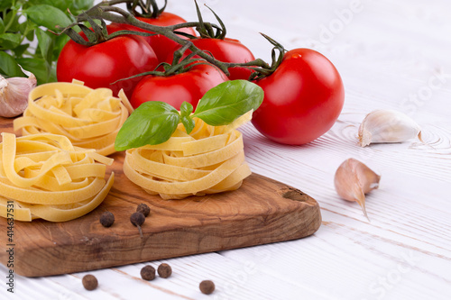 Raw tagliatelle pasta with fresh basil, garlic and tomatoes on a rustic white table, Copy space