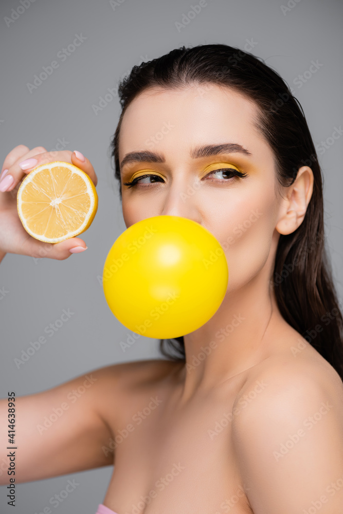 young woman with makeup blowing yellow bubblegum and holding half of lemon isolated on grey young woman with makeup blowing yellow bubblegum and holding half of lemon isolated on grey