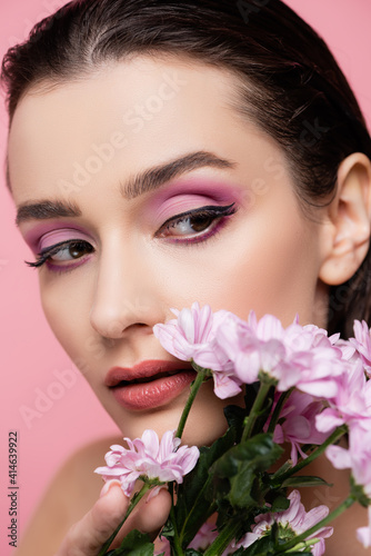 close up of young sensual woman looking away near flowers isolated on pink