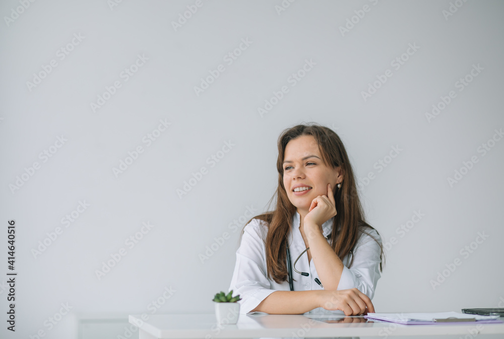 Smiling female physician posing while sitting at the table in hospital office. Medicine concept Smiling female physician posing while sitting at the table in hospital office. Medicine concept
