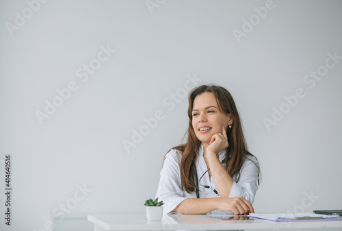 Smiling female physician posing while sitting at the table in hospital office. Medicine concept