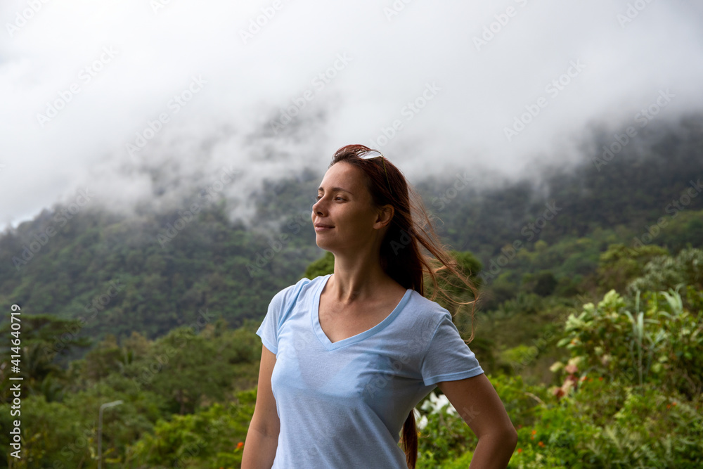 Naklejka premium Happy woman portrait in mountain landscape with white clouds. Candid face portrait on top of mountain. Female tourist in natural environment. Hiking and trekking concept. Cloudy forest landscape