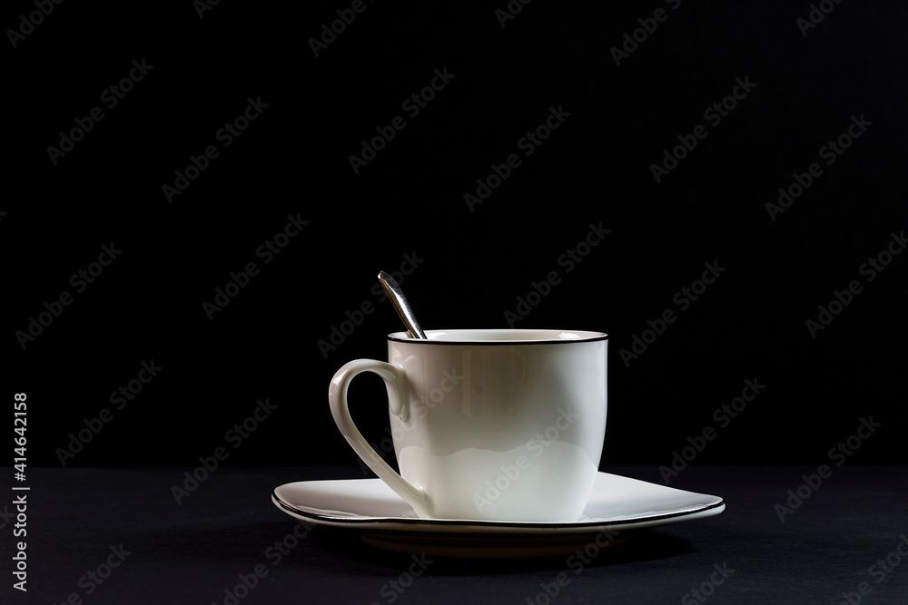 Porcelain spoon, cup and plate on black background. The photograph is a horizontal shot taken in a studio under artificial lighting. Porcelain spoon, cup and plate on black background. The photograph is a horizontal shot taken in a studio under artificial lighting.