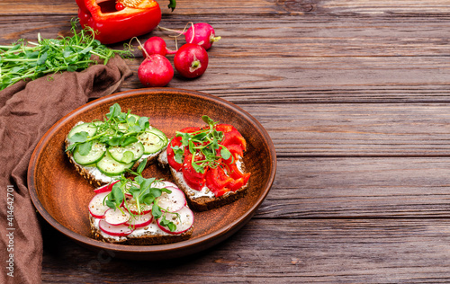 Different sandwiches with cucumber, radish, red paprika and microgreens on a plate on a wooden background.