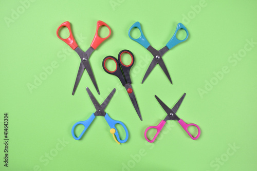 Opened scissors in red blue pink and black color scattered on green background