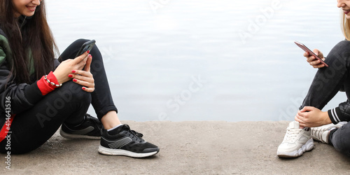 Legs of two young stylish hipster girls writing messages on smartphone. Girls is sitting and communicate in social networks. The concept of teenagers  students  modern technology. Panorama