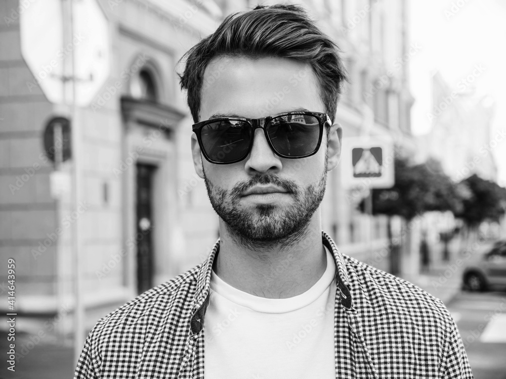 Portrait of handsome smiling stylish hipster lambersexual model.Man dressed in white T-shirt. Fashion male posing in the street in sunglasses