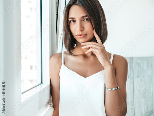 Portrait of beautiful woman dressed in white pajamas. Sexy carefree model enjoying her morning at balcony. She dreams about something and looking out the window. Female in her thoughts