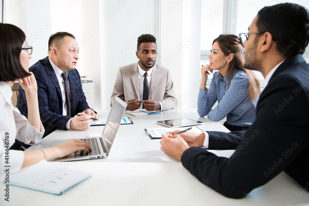 Group of business people sitting around the office desk and discussing the project Group of business people sitting around the office desk and discussing the project