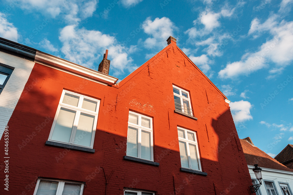 Close-up of a red vibrant color facade made of bricks against the blue sky in Bruges, Belgium.