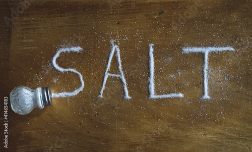 Salt shaker and grains of salt on a wooden surface forming the word "salt".