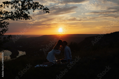 Silhouette of sensual young couple in love kissing at the summer picnic at amazing sunset.