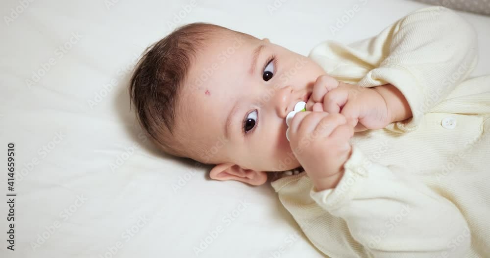 Newborn cheerful littlebaby is chewing and playing in his crib with nipple. Funny smiling looks through the railing of the crib. slow motion Newborn cheerful littlebaby is chewing and playing in his crib with nipple. Funny smiling looks through the railing of the crib. slow motion