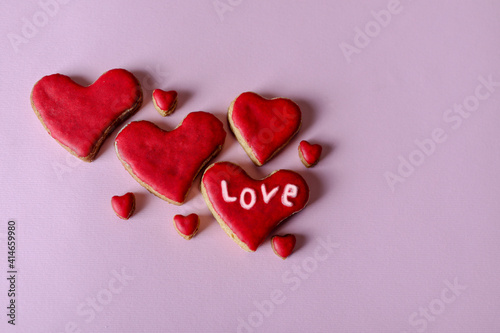 Cute hand made red cookies in the shape of a heart with word love isolated on purple background with copy space for text or design. Valentines day and love concept © Emilija