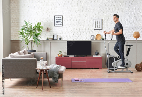 Man is doing sport at home, fit male training style, decorative living room, brick wall sofa and television unit style.