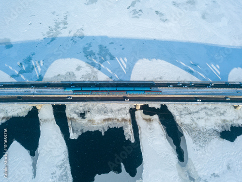 Two metro trains travel on Kiev metro bridge. A shadow falls on the frozen Dnieper River. Aerial drone view. Winter sunny morning.