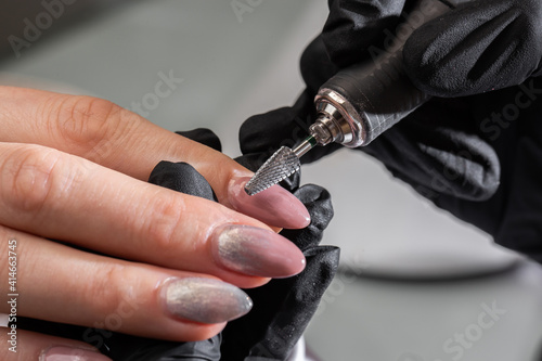 Hardware manicure process in a beauty salon. Close-up of manicurist s hands in black gloves using automatic electric manicure drill to remove nail polish from client s nails. Manicure care procedure.