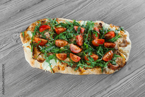 Scrocchiarella gourmet italian cuisine on grey wooden background. Pinsa romana traditional dish. Food delivery from pizzeria. Pinsa with meat, arugula, tomatoes, cheese. photo