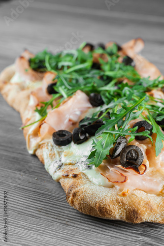 Pinsa romana gourmet italian cuisine on grey wooden background. Scrocchiarella traditional dish. Food delivery from pizzeria. Pinsa with meat, arugula, olives, cheese. photo