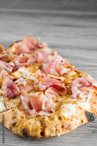 Scrocchiarella with pear, cheese, prosciutto on grey wooden background. Pinsa romana gourmet italian cuisine. Food delivery from pizzeria. Junk food photo