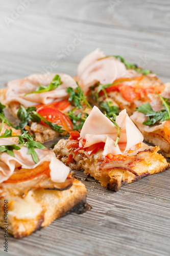 Pinsa romana cut into pieces portions for one person. Food delivery from pizzeria. Pinsa with meat, arugula, cheese. Scrocchiarella gourmet italian cuisine on grey wooden background.