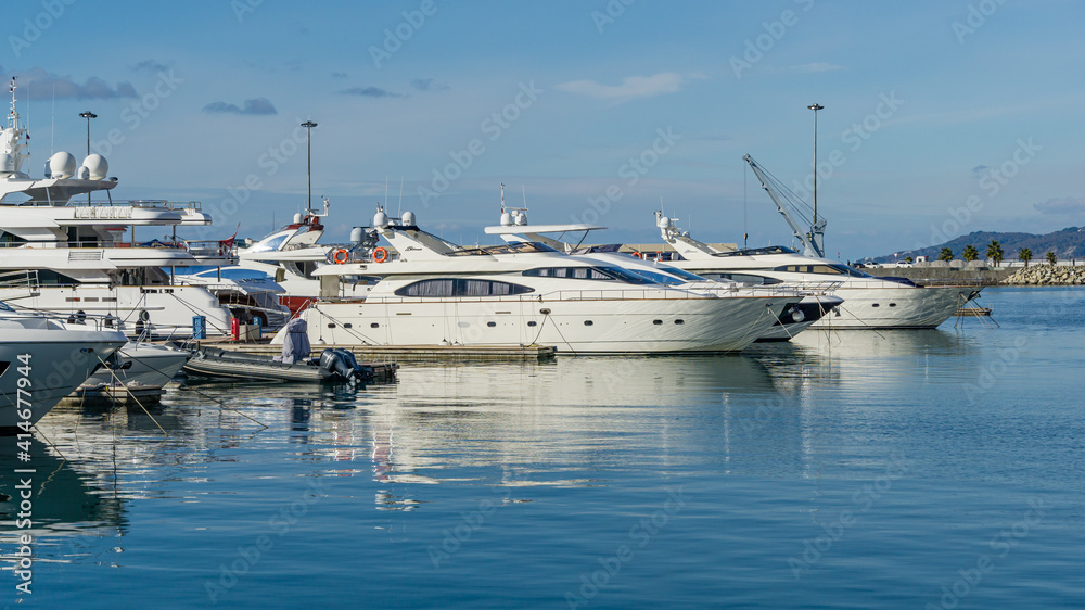 Ships, yachts and boats on blue surface of Black Sea by pier of Commercial seaport of Sochi. Resort city center. Sochi, Russia - November 23, 2020