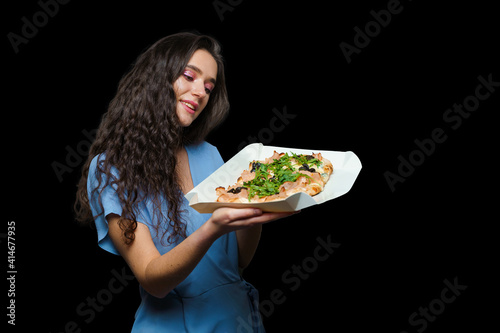 Woman courier with pinsa romana gourmet italian cuisine on black background. Holding scrocchiarella traditional dish. Food delivery from pizzeria. Pinsa with meat, arugula, olives, cheese. photo