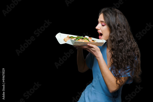 Woman courier with pinsa romana gourmet italian cuisine on black background. Holding scrocchiarella traditional dish. Food delivery from pizzeria. Pinsa with meat, arugula, olives, cheese. photo