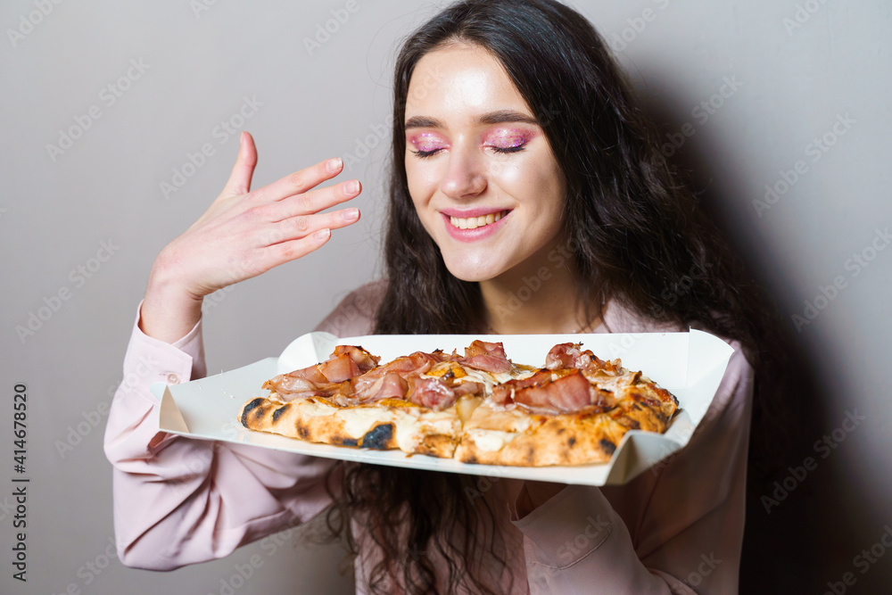 Girl courier with pinsa romana gourmet italian cuisine on grey background. Holding scrocchiarella traditional dish. Food delivery from pizzeria. Pinsa with meat, arugula, olives, cheese.