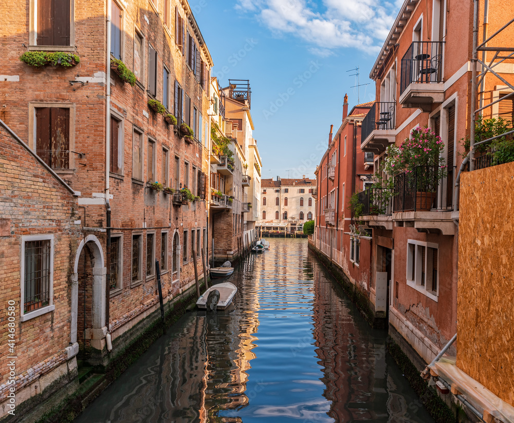 View of calm canal and cozy street with flowers on the balconies of the residential area of Venice, Italy.