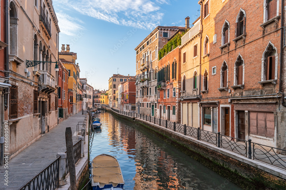 View of cozy street and calm canal with boats along brink. The residential area of Venice, Italy.