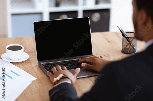 Black businessman hands typing on laptop with blank screen
