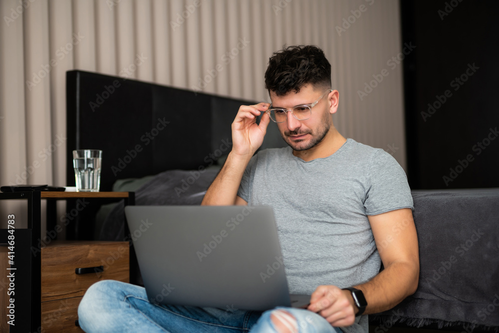 Handsome young man using laptop while sitting on floor in bedroom Handsome young man using laptop while sitting on floor in bedroom