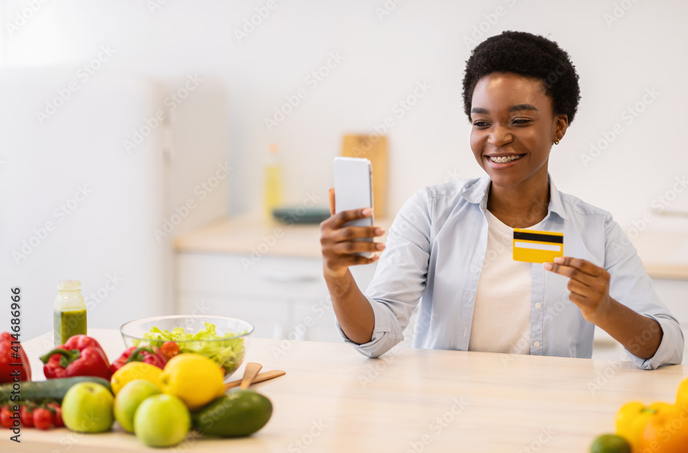 Obraz premium Woman Using Phone Grocery Shopping Application Holding Credit Card Indoor