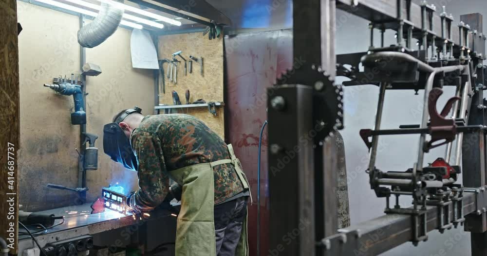 A male master welder performs the welding process. The process of welding spare parts for electric bicycles in a tilting mask in the workshop of spark engineering A male master welder performs the welding process. The process of welding spare parts for electric bicycles in a tilting mask in the workshop of spark engineering