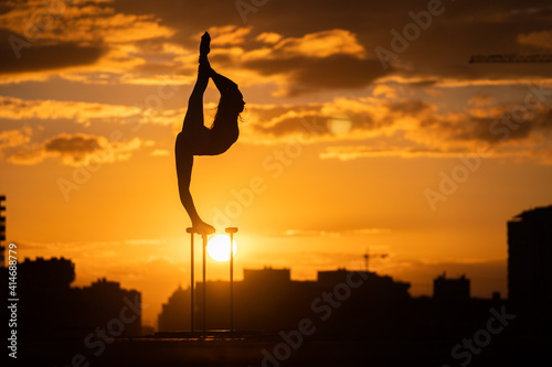 Flexible acrobat doing handstand on the cityscape background during dramatic sunset. Concept of willpower, control and dream