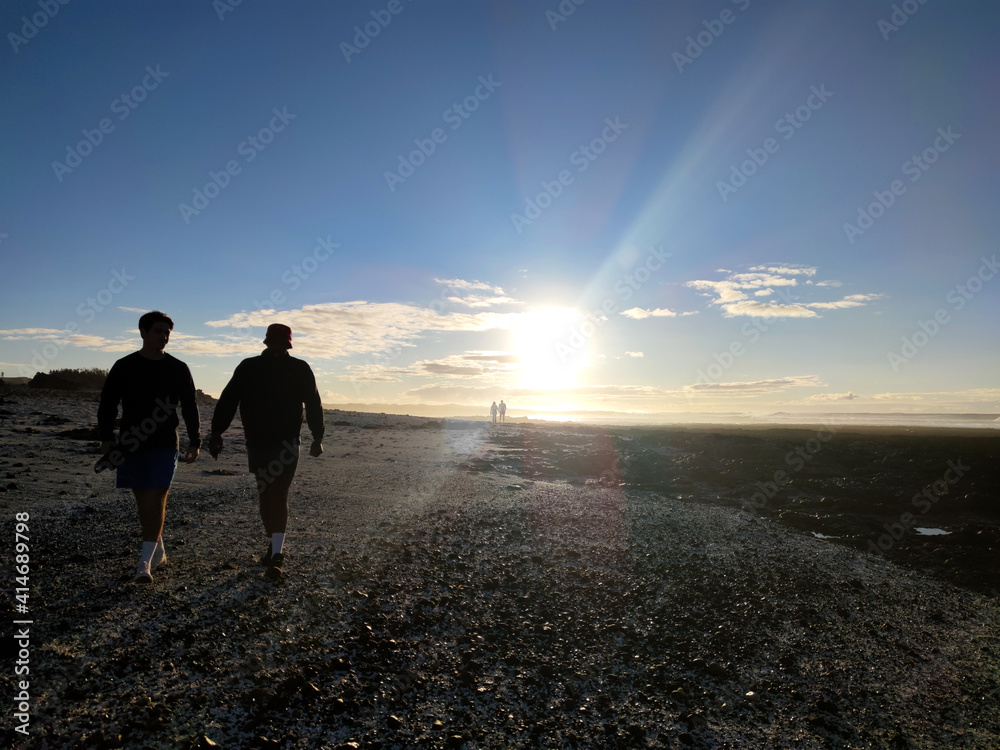Silhouette of two man walking on a pebble beach