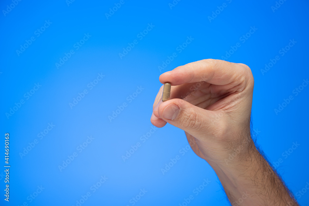 Gray capsule medical pill held between fingers by Caucasian male hand isolate on blue background studio shot Gray capsule medical pill held between fingers by Caucasian male hand isolate on blue background studio shot