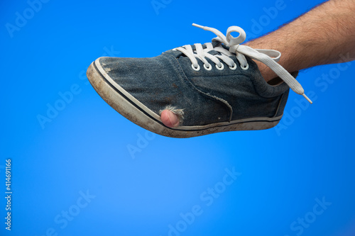 Caucasian male hand holding a pair of worn out dirty old textile shoes finger pocking out of hole isolated on blue background studio shot