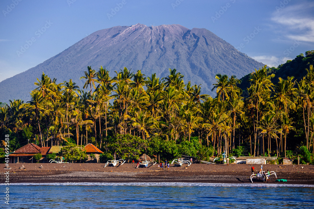 Agung volcano in Bali Indonesia from the sea with palm trees and fisherman boats 